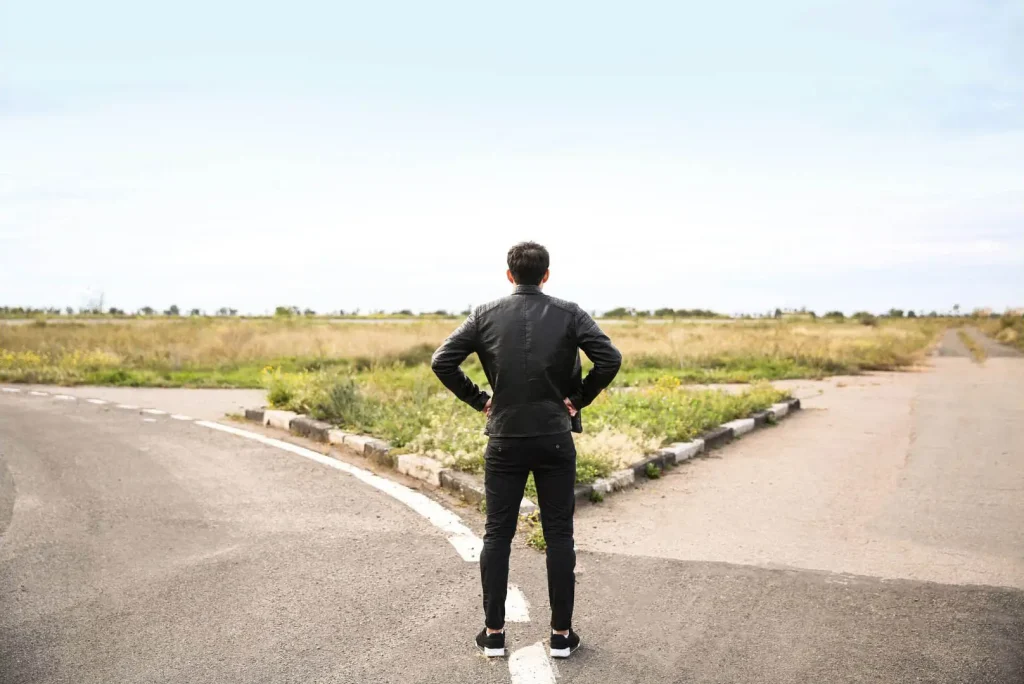 A man in black clothing standing at a crossroads on a sunny day