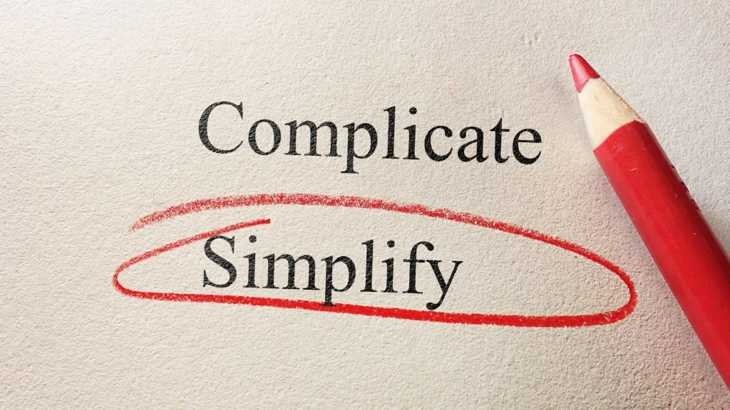 The word "Complicate" appears above "Simplify," which is circled in red pencil on a page, with the red pencil pointing at the circled word, symbolizing how small business funding can be simplified.